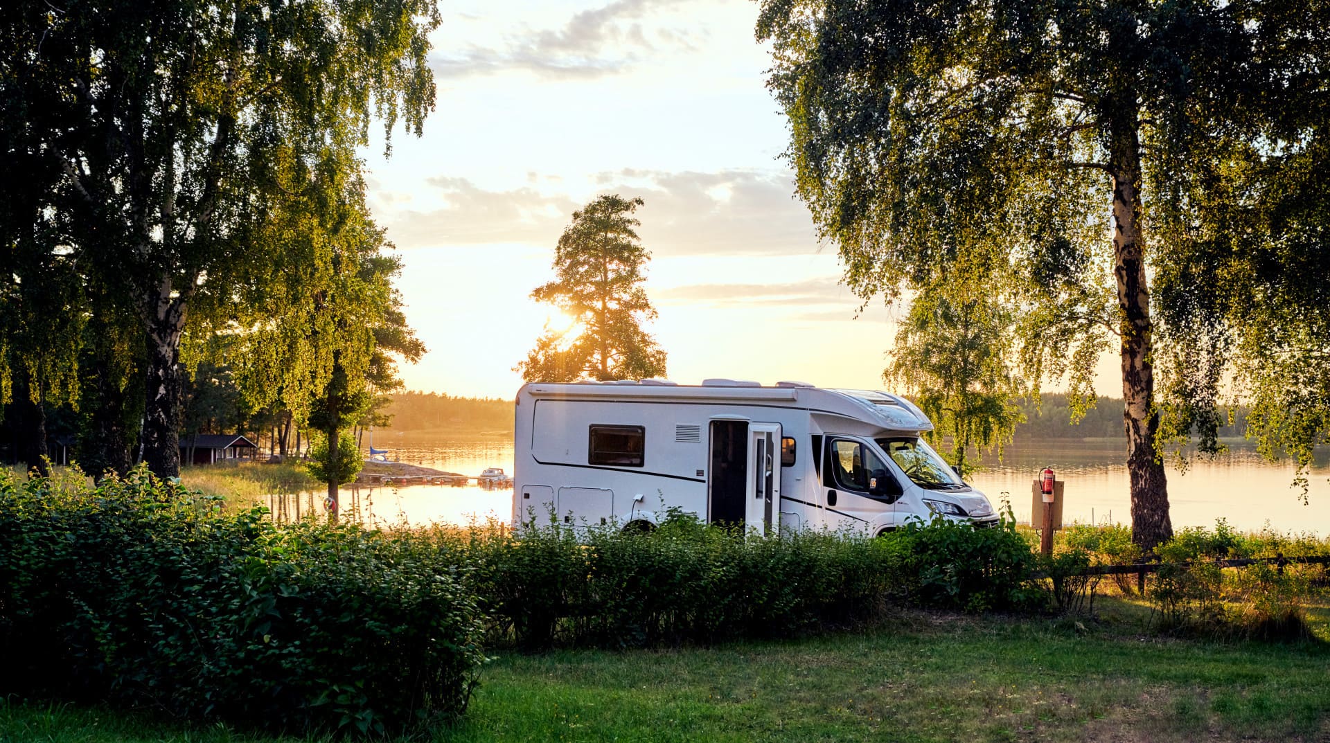A motorhome near a lake and trees at sunset